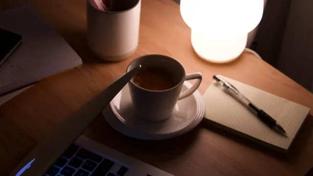 Cup of tea beside a notebook under a warm desk lamp