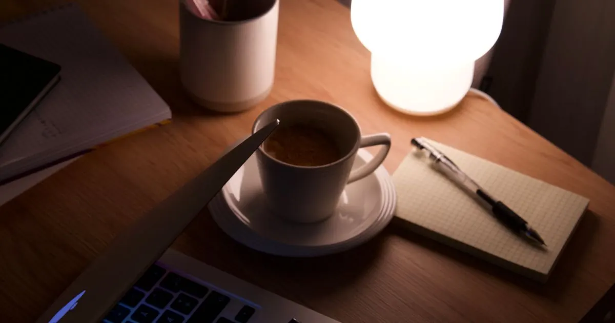 Cup of tea beside a notebook under a warm desk lamp