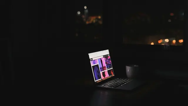 Laptop glowing on a desk in a dark room at night