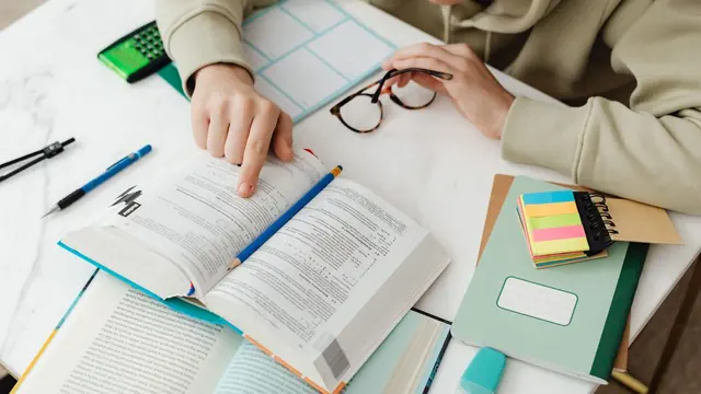 Student highlighting a textbook on a desk with sticky notes and a calculator