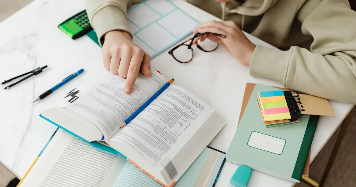 Student highlighting a textbook on a desk with sticky notes and a calculator