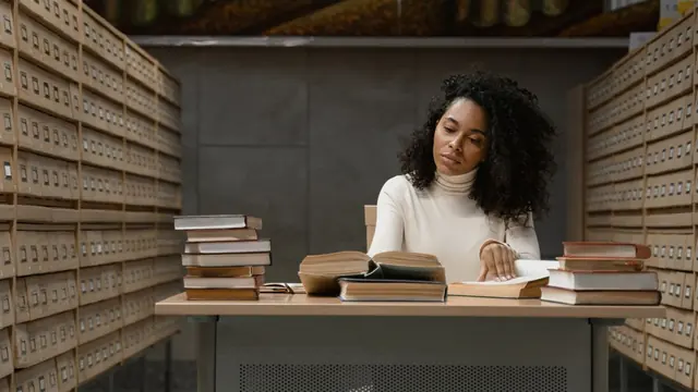 Student reading at a desk stacked with books in a library archive