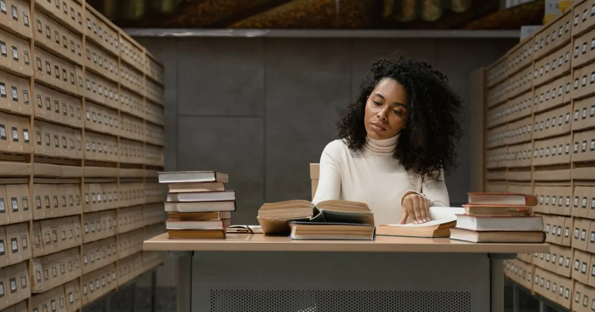 Student reading at a desk stacked with books in a library archive