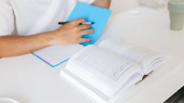 Student writing revision notes next to an open textbook