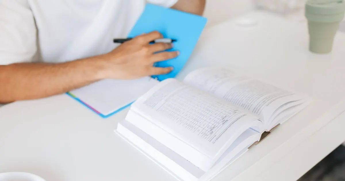 Student writing revision notes next to an open textbook