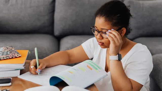 Student writing notes at home with her head resting on her hand