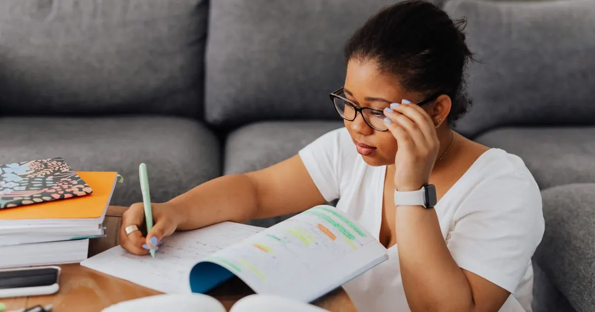 Student writing notes at home with her head resting on her hand