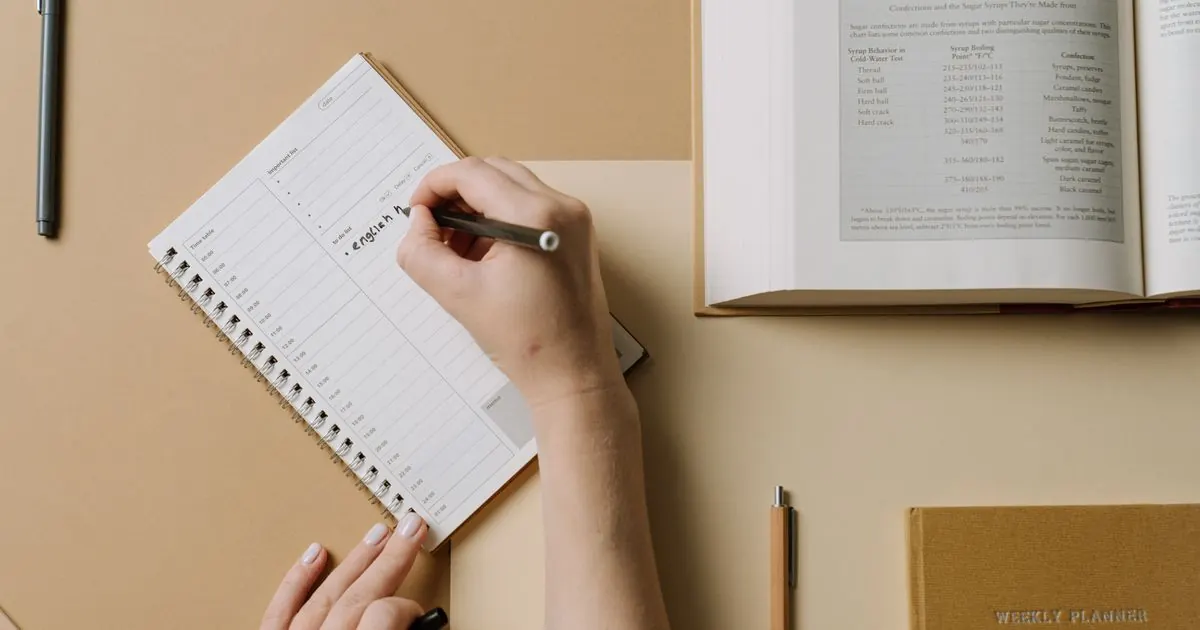 Hand writing a weekly study plan in a spiral notebook