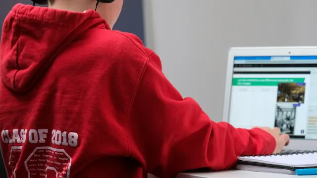 Student in a red hoodie working on a laptop