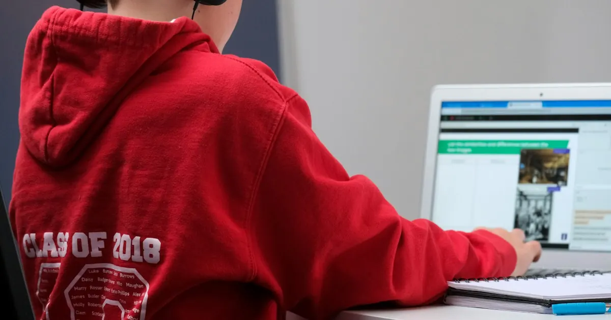 Student in a red hoodie working on a laptop