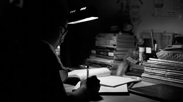 Student studying alone at night under a single desk lamp