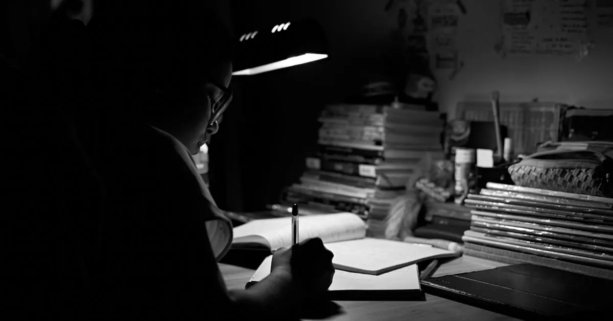 Student studying alone at night under a single desk lamp