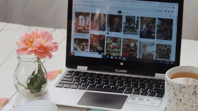 Laptop on a white desk with a cup of tea and pink flowers