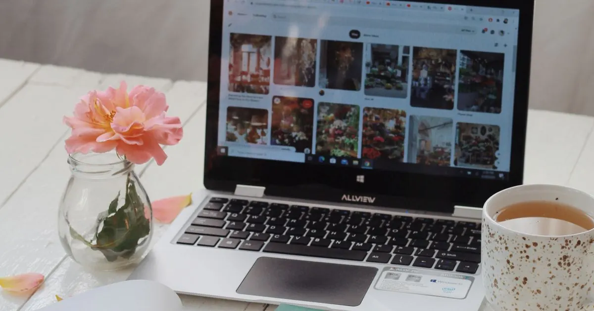 Laptop on a white desk with a cup of tea and pink flowers